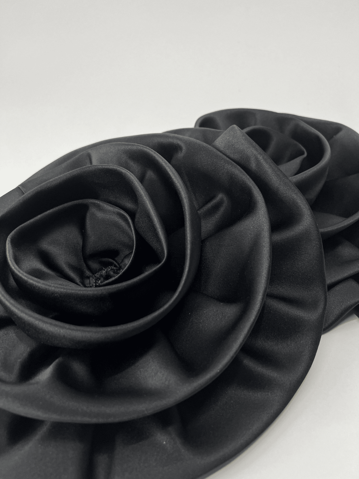 Flat lay of Ceva Camellia Flower Satin Gloves in black, showcasing the luxurious satin texture and floral embellishment.