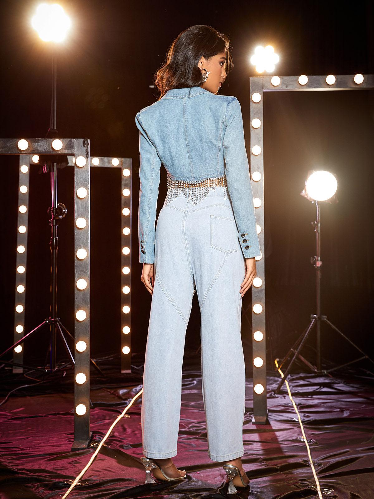 A model wears a blue denim chain fringe blazer. The modern silhouette features an open front and long sleeves.  The jacket has a stylish chain fringe detail. Perfect for layering.