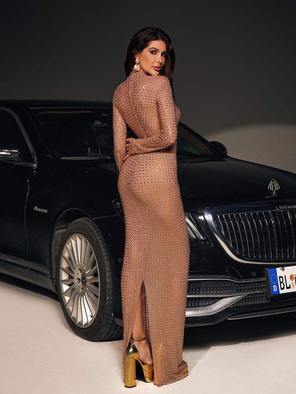 A breathtaking model in a luxurious gold Karter diamond mesh maxi dress.  The dress features long sleeves, a thigh-high slit, and exquisite rhinestone embellishments. Perfect for a special occasion.
